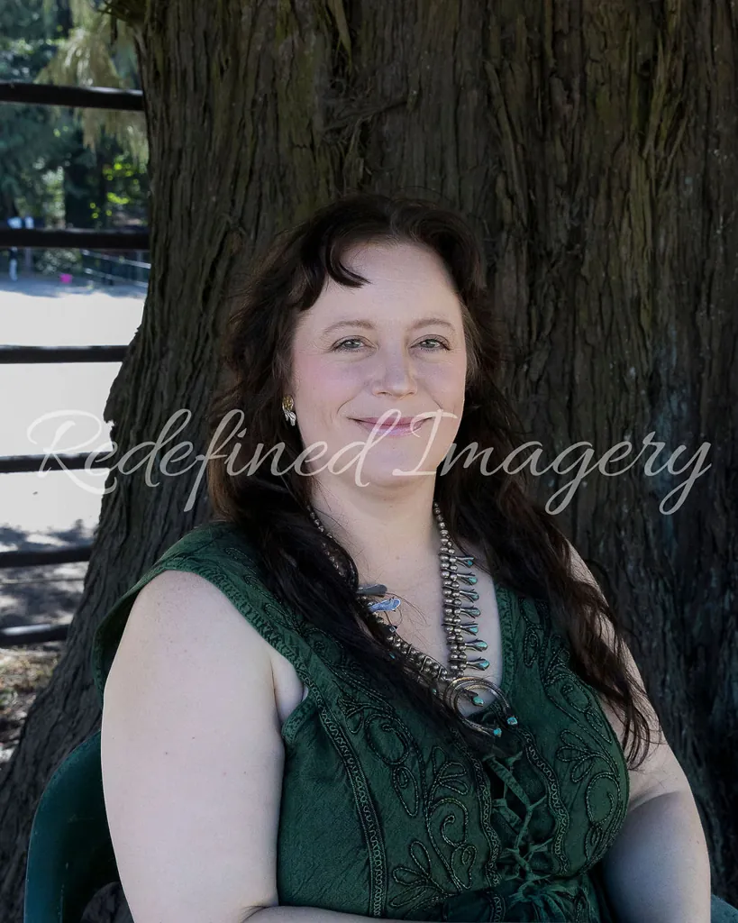 Morgan Nilsen smiling, seated in front of a large tree trunk